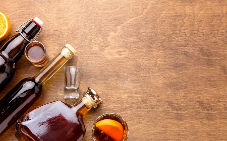 Бутылки с алкоголем, стопка и дольки апельсина на деревянном столе